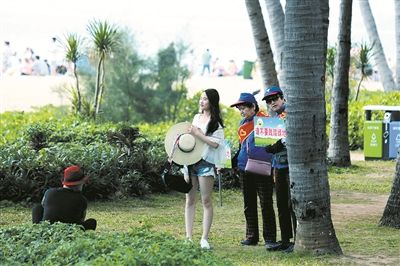 三亚绿地上，志愿者举着牌子，劝导游客别踩踏草地